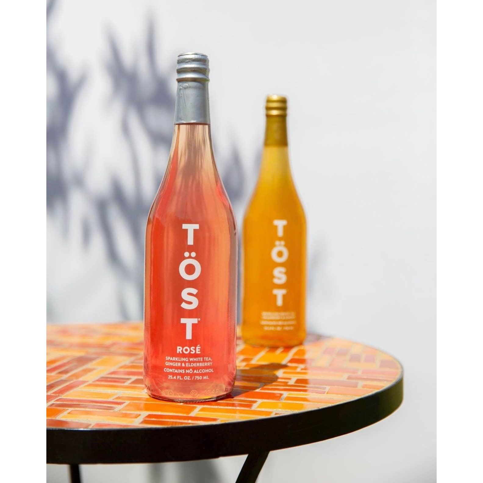 Two bottles of TÖST ROSÉ a Non-Alcoholic Refresher, one from TÖST Beverages and one original, on a small round table with a mosaic pattern.