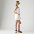 A person stands in profile against a plain background, wearing a white tank top, Levi's High Baggy Short with a vintage-inspired fit, and black strappy sandals.