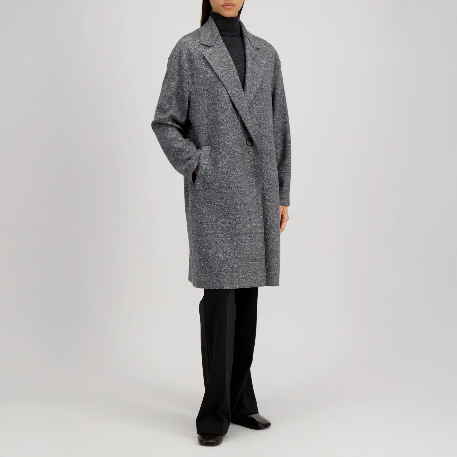 A person wears the Harris Wharf W Oversized Coat Donegal in grey, paired with a black turtleneck, black trousers, and shoes, standing against a plain light background.