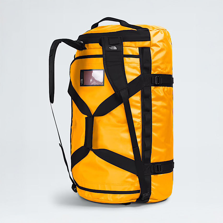 The North Face Base Camp Duffel L in Summit Gold stands upright with black straps, handles, and buckles on a plain background, highlighting its rugged durability as the ultimate travel bag.