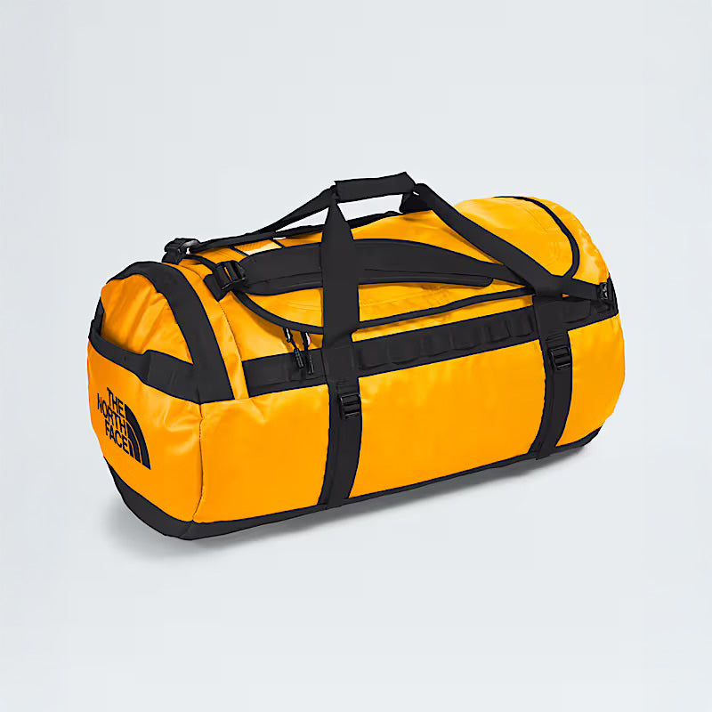 A Summit Gold Base Camp Duffel L by The North Face, featuring handles and adjustable straps, known for its rugged durability, is placed on a plain light background.