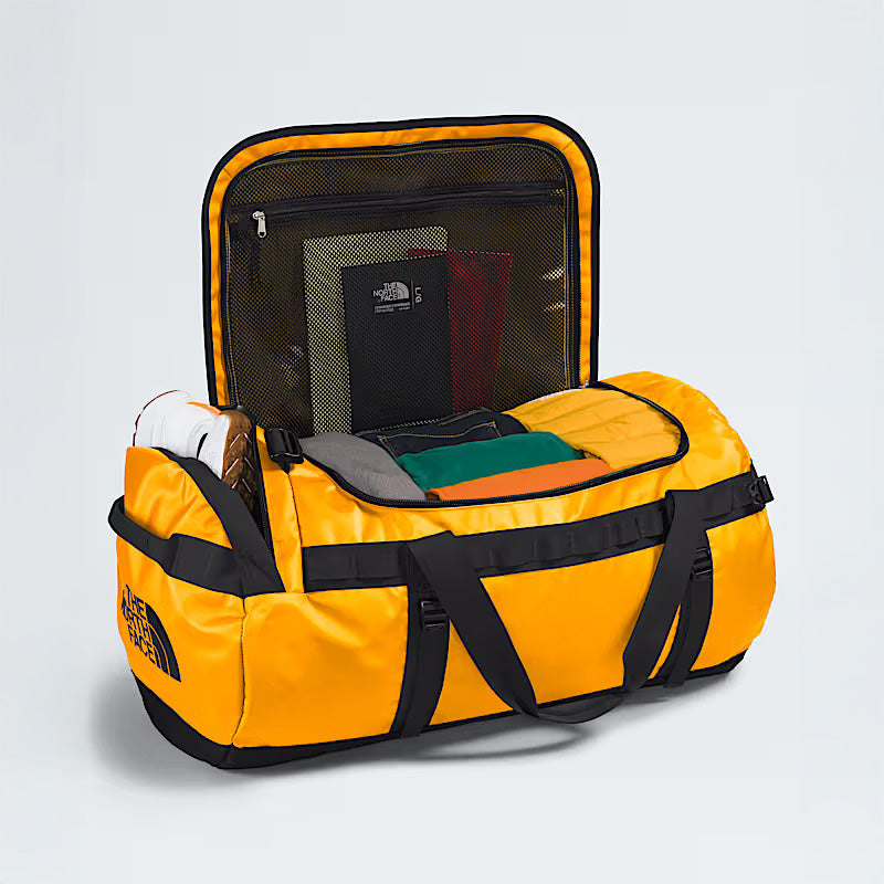 A Summit Gold Base Camp Duffel L by The North Face with black straps sits open to display neatly packed clothes and mesh lid compartments—ideal for travelers who appreciate rugged durability in a bag.