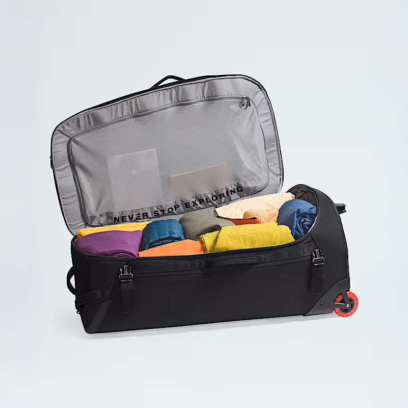 A black The North Face Base Camp Rolling Thunder 36 Luggage sits open, revealing neatly packed colorful clothes and two books in the mesh-lined lid. Crafted from recycled fabric, it features a tough hard-shell chassis for extra protection.