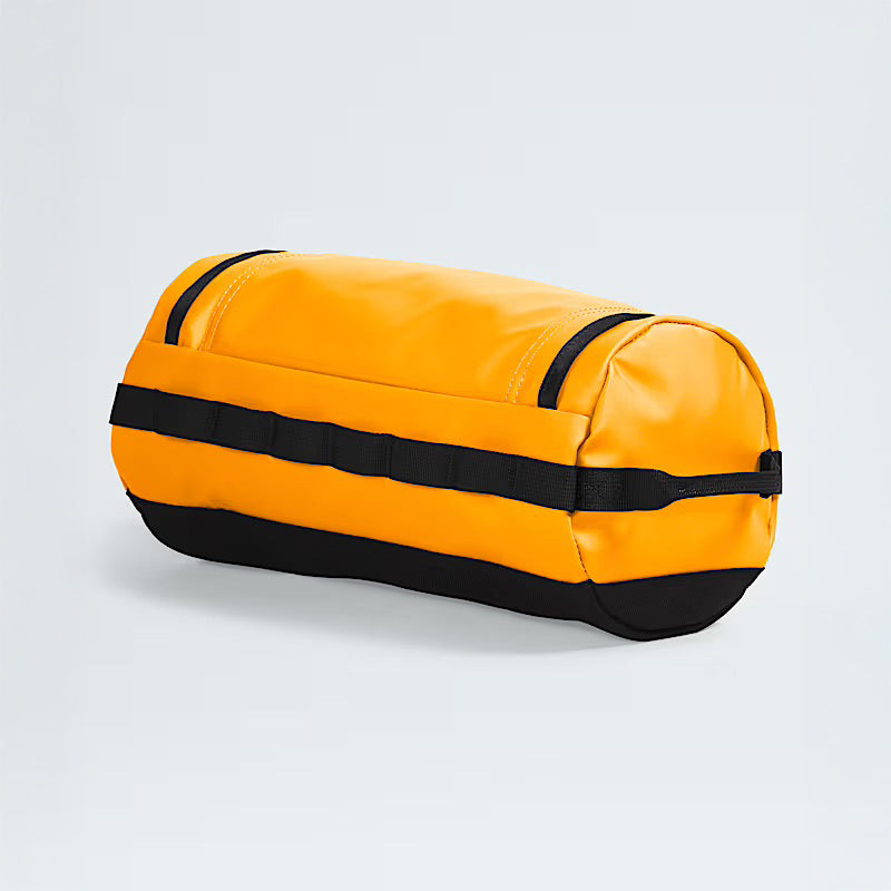 The North Face Base Camp Travel Canister in Summit Gold, featuring black handle straps, is displayed on a light gray background—an ideal and durable carry-all for your essentials.