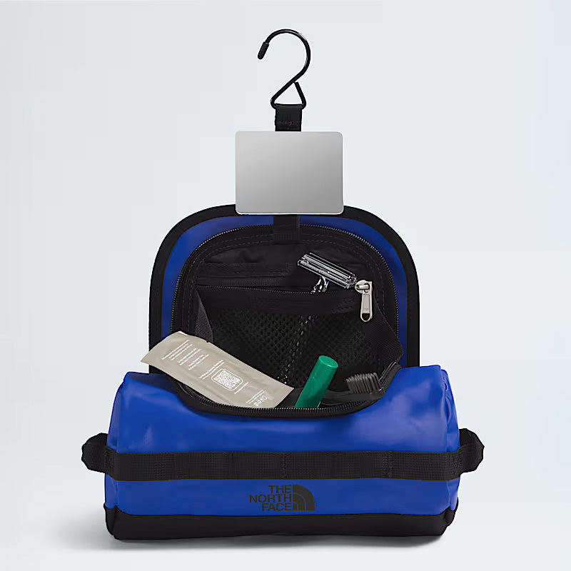 The North Face Base Camp Travel Canister S in blue, made from recycled materials, features a hook, mesh pocket, small mirror, and includes various personal care items inside.