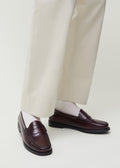 A person wearing cream-colored trousers and dark brown loafers, paired with Aiayu's Cotton Rib Socks in white, made in Europe from GOTS-certified organic cotton.