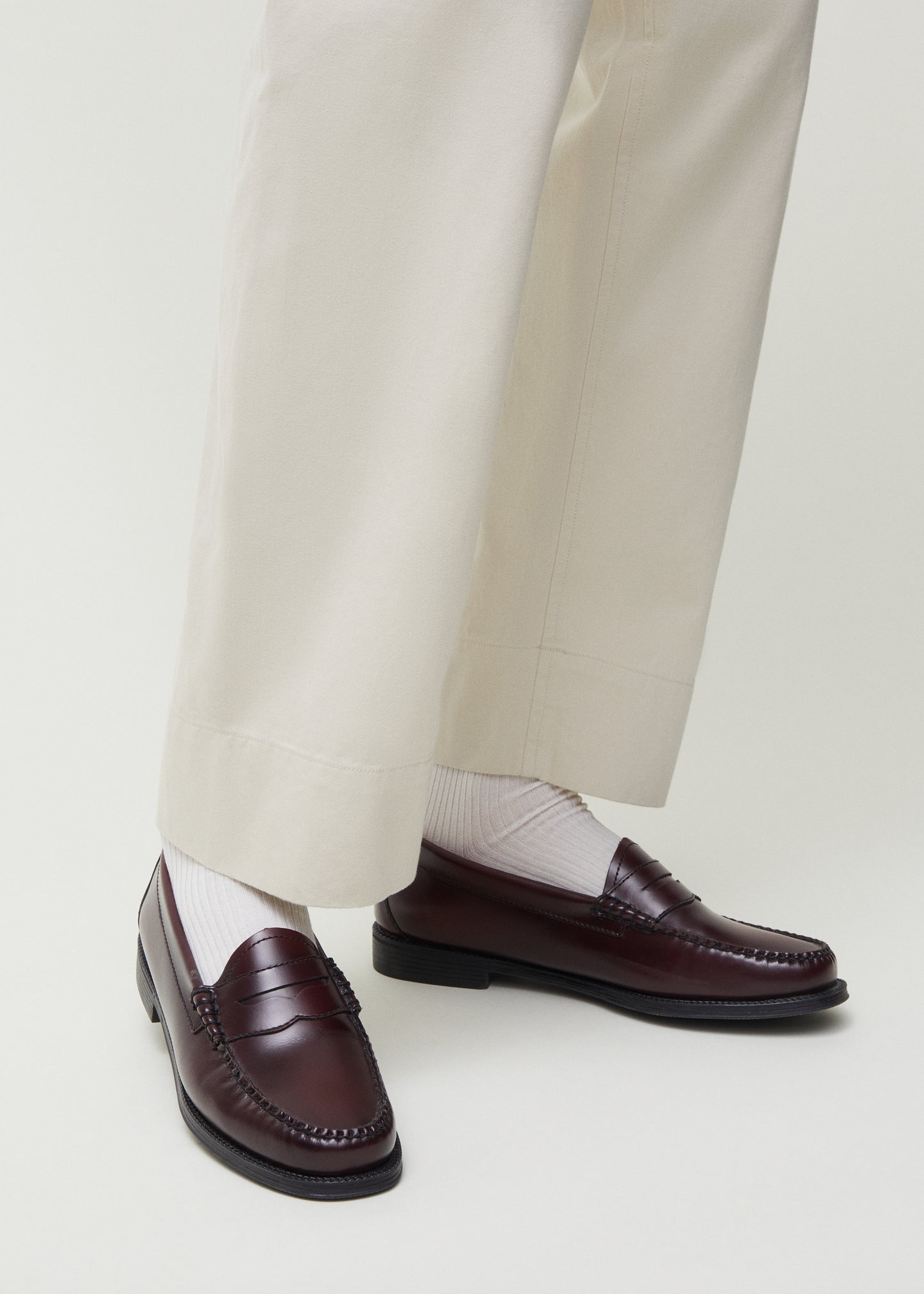 A person wearing cream-colored trousers and dark brown loafers, paired with Aiayu's Cotton Rib Socks in white, made in Europe from GOTS-certified organic cotton.