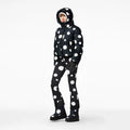 A person stands against a plain background wearing Goldbergh's Grand Ski Jacket in Dot Black, featuring large white polka dots, with matching pants and boots.