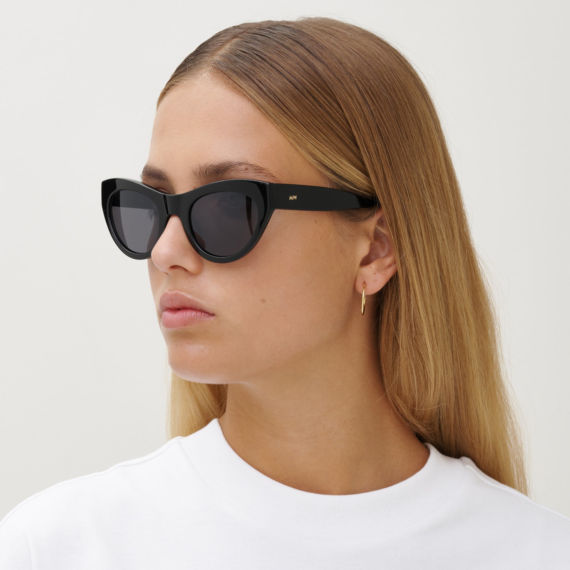 A woman with straight, light brown hair wears Messyweekend Donna sunglasses in Grey/Black and a white top, looking to the side against a plain background.