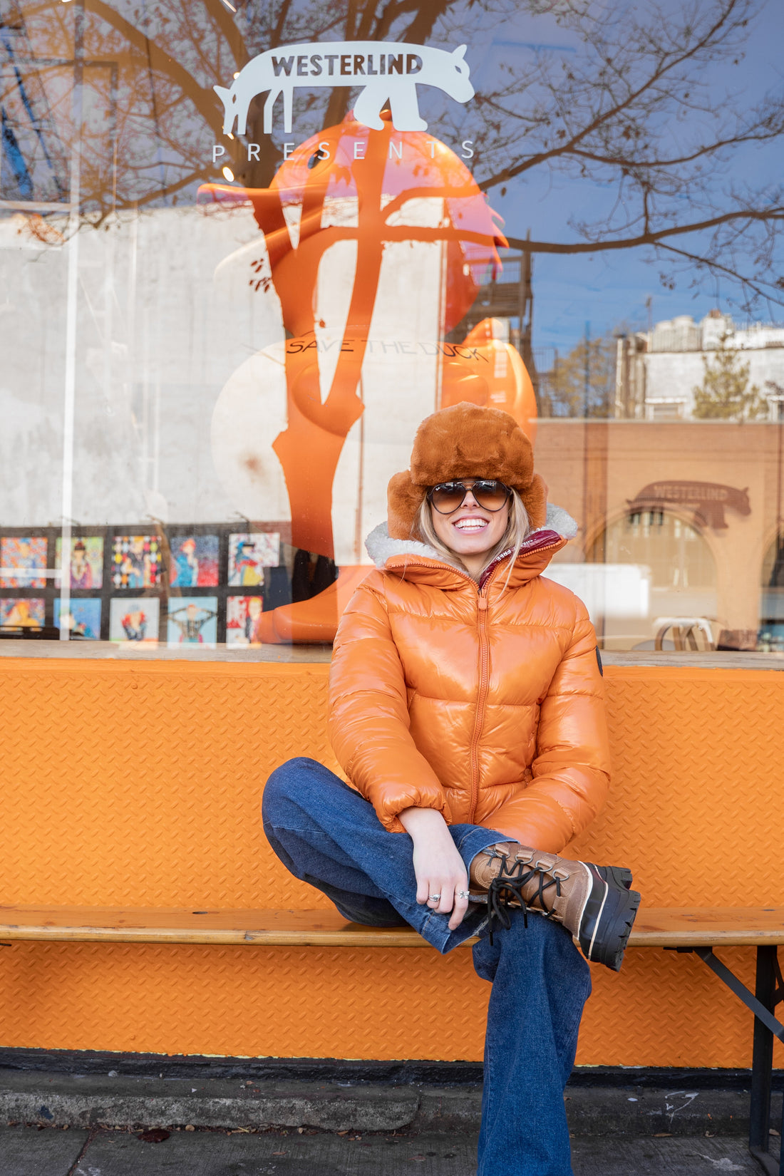 Person wearing an orange coat sitting on a bench with a store window in the background