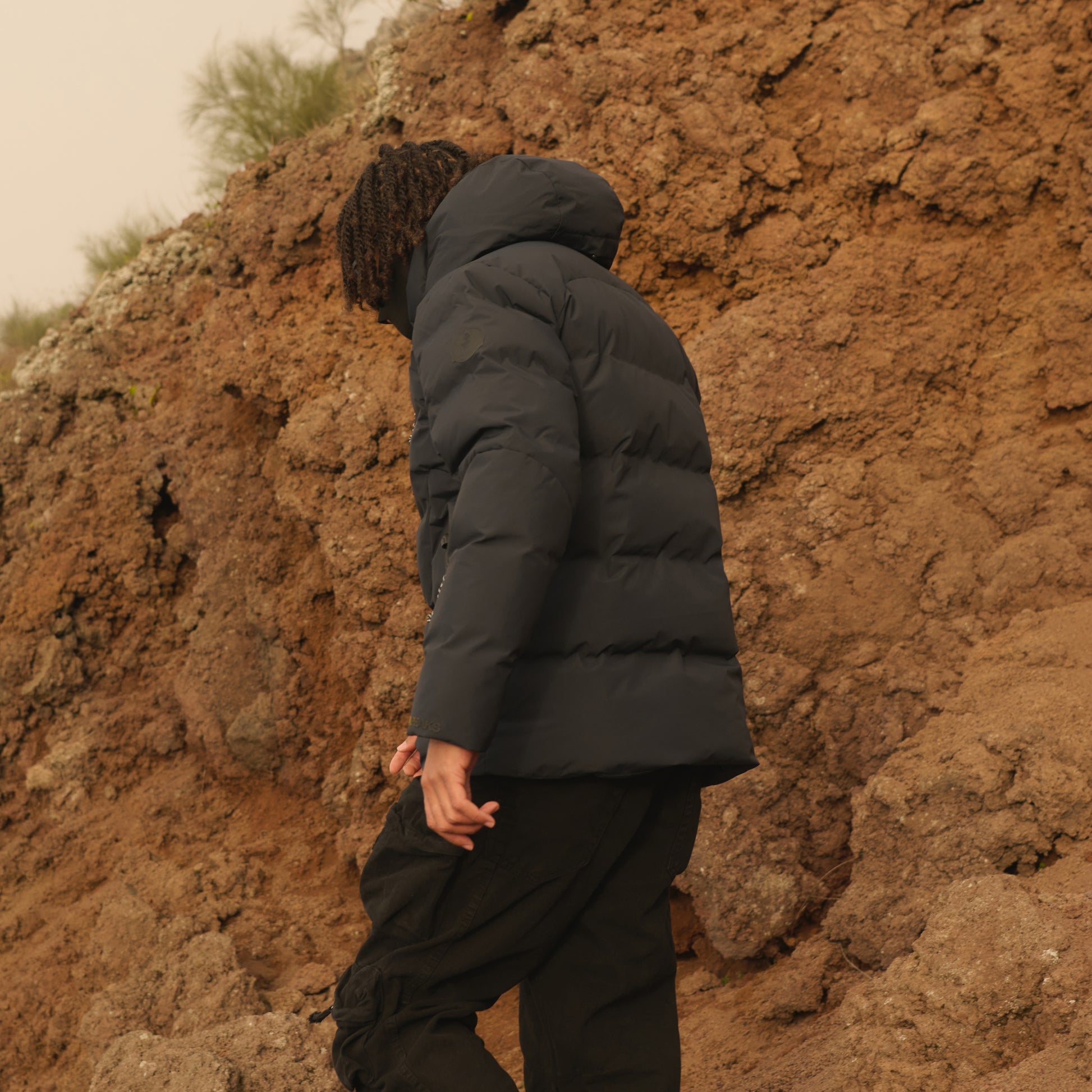 Person wearing a black puffer jacket against a rocky wall
