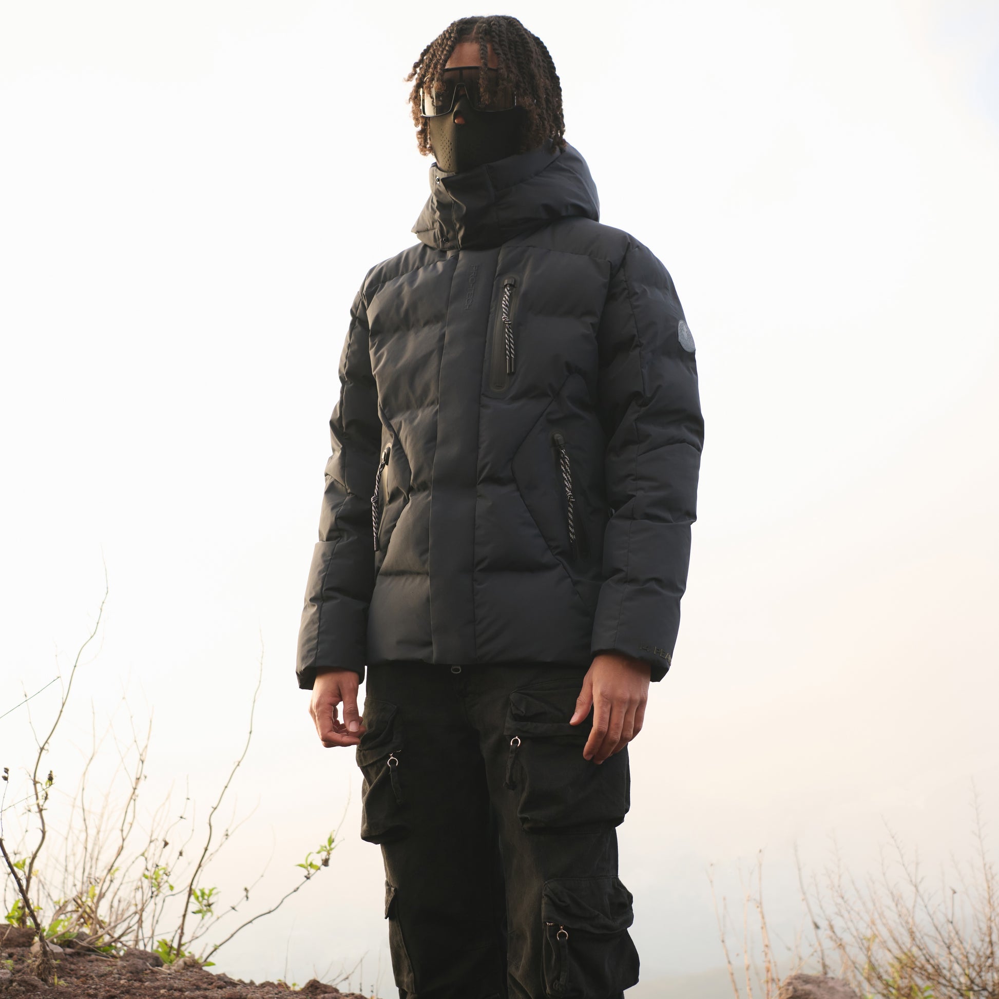 Person wearing a black puffer jacket and pants in a natural setting