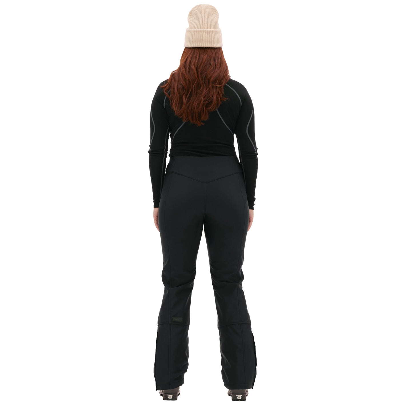 A person in black skiing attire and a beige beanie faces away, showcasing the sleek design of Halfdays' Emma Pant, highlighting the back of their outfit.