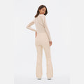 Dressed in a beige, slim-fit ensemble, including the Halfdays Emma Pant with flared bottoms and a matching long-sleeve top, this person stands sideways, poised to conquer the slopes.