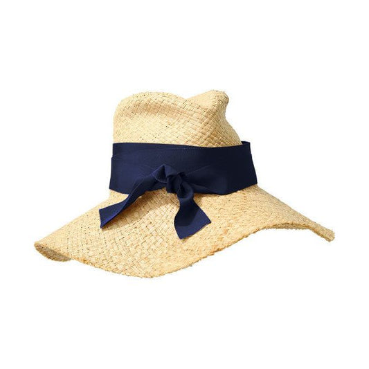 A straw hat made from raffia material, featuring a wide brim and a dark blue adaptable ribbon tied around it, perfect for summer style. The **First Aid, Nude w/ Navy** by **Lola Hats**.