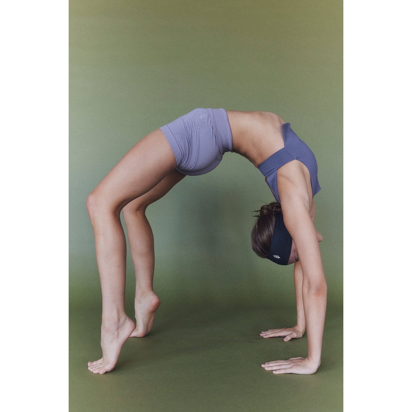 A person in Free People Movement's gray and blue Be Right Back Cami performing a backbend on a green background.