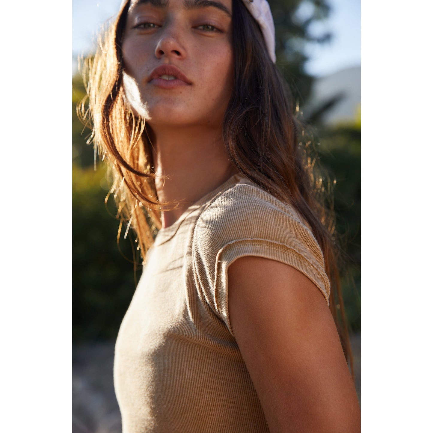 Close-up of a young woman in a Ribbed Baby Tee by Free People Movement, wearing a headband, with sunlight highlighting her hair and face.