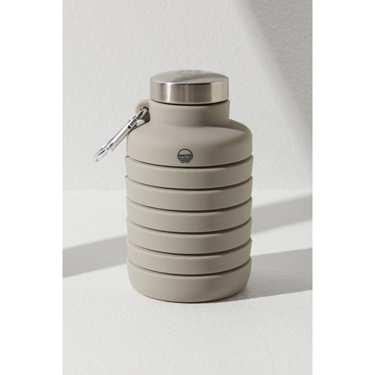 A collapsible, gray silicone 24OZ Carabiner Bottle by Free People Movement with a stainless steel cap and a carabiner attached, displayed against a white textured background.
