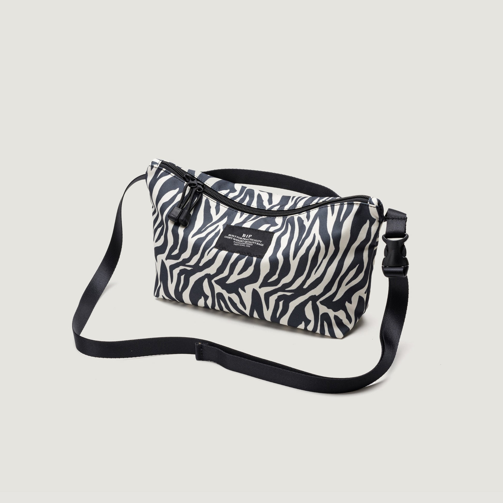 The Bags in Progress Fannypack Crossbody is a small shoulder bag made from recycled polyester, featuring a black and white zebra print, adjustable black strap, and water-repellent finish. Shown on a light background.