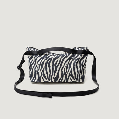 A Fannypack Crossbody with a zebra print design on a light background, featuring a black adjustable strap and black accents by Bags in Progress.