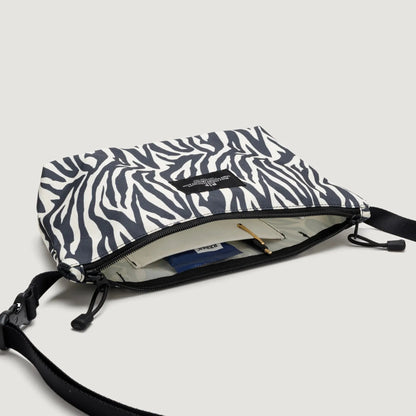 A Fannypack Crossbody, Zebra bag from Bags in Progress with an open zipper showing contents including a notebook and passport.