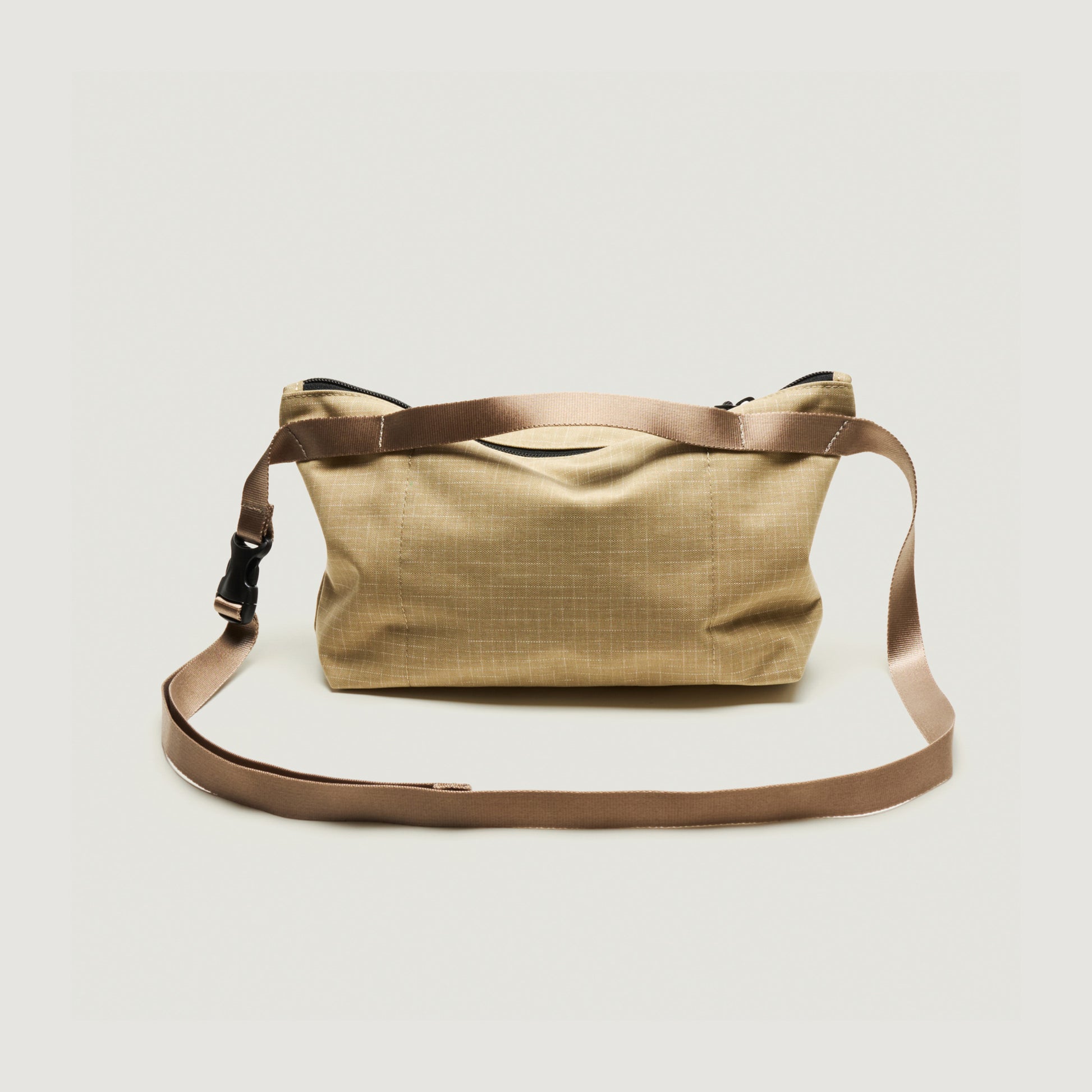 The Bags in Progress Fannypack Crossbody is a beige recycled polyester shoulder bag with a brown adjustable strap and zippered top, shown against a plain white background.