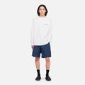 A person stands facing forward, wearing a white long-sleeve shirt and Gramicci's Nylon Loose Short in navy blue, which are water-repellent and wind-resistant, paired with black socks and sandals against a plain white background.