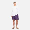 A person stands facing forward against a plain background, wearing a light-colored cap, white long-sleeve shirt, Gramicci Nylon Loose Short in purple, and brown sandals.