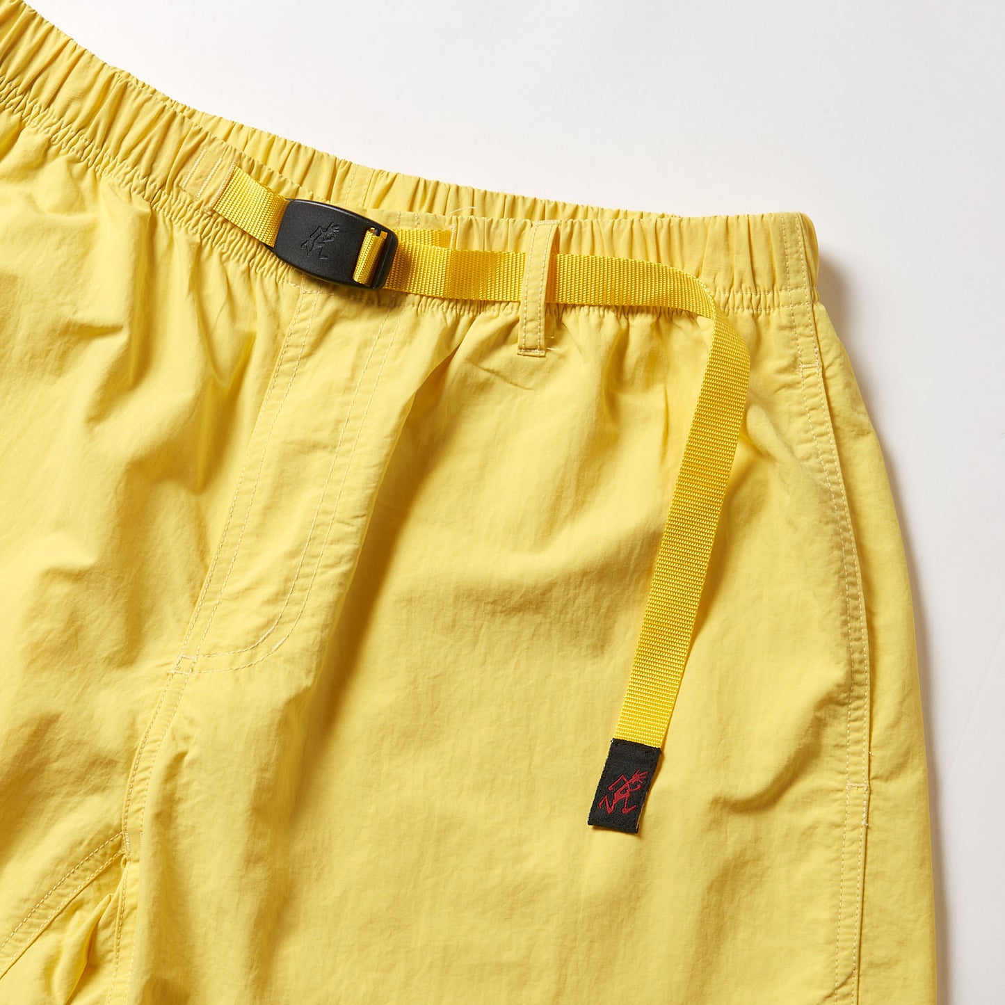 The Gramicci Nylon Loose Short in yellow, with an elastic waistband, adjustable webbing belt, front pocket detail, and water-repellent, wind-resistant properties, is shown laid flat on a white surface.