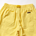The Gramicci Nylon Loose Short features yellow nylon fabric, an elastic waistband, two large back pockets, a black and red label at the right waist, and is water-repellent for versatile wear.
