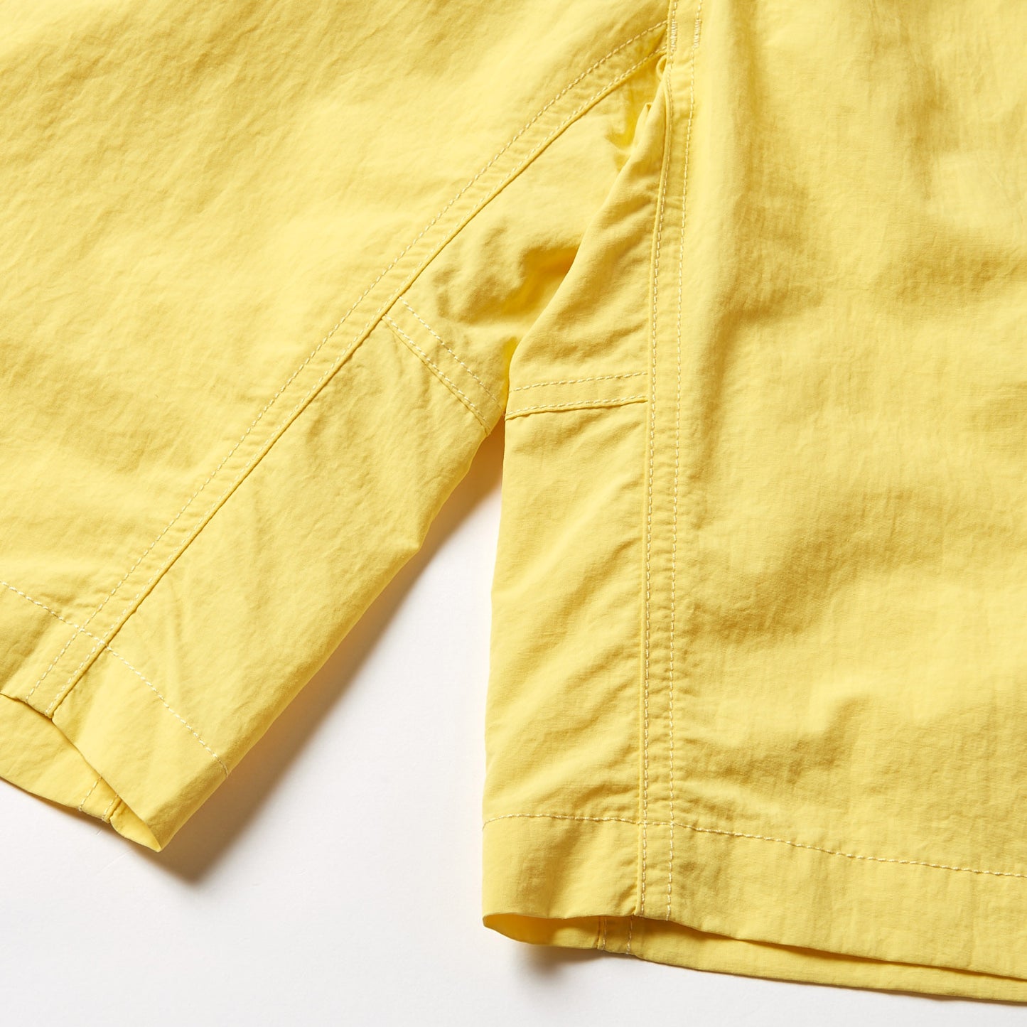 Close-up of the hem and side seam on Gramicci's Nylon Loose Short, showcasing detailed stitching, wind-resistant yellow nylon fabric, and subtle texture.