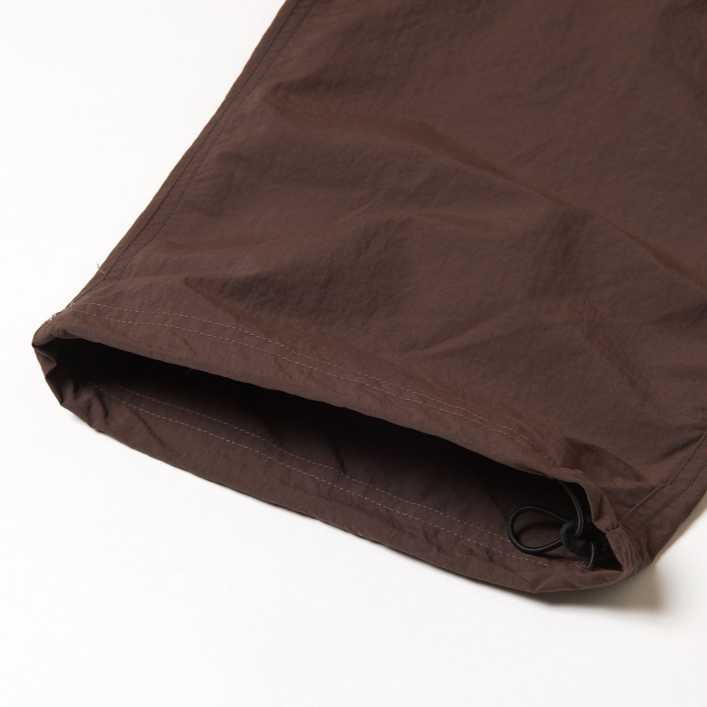 A close-up of the hem of Gramicci Nylon Runners in brown, featuring an adjustable drawstring, shown on a white background.