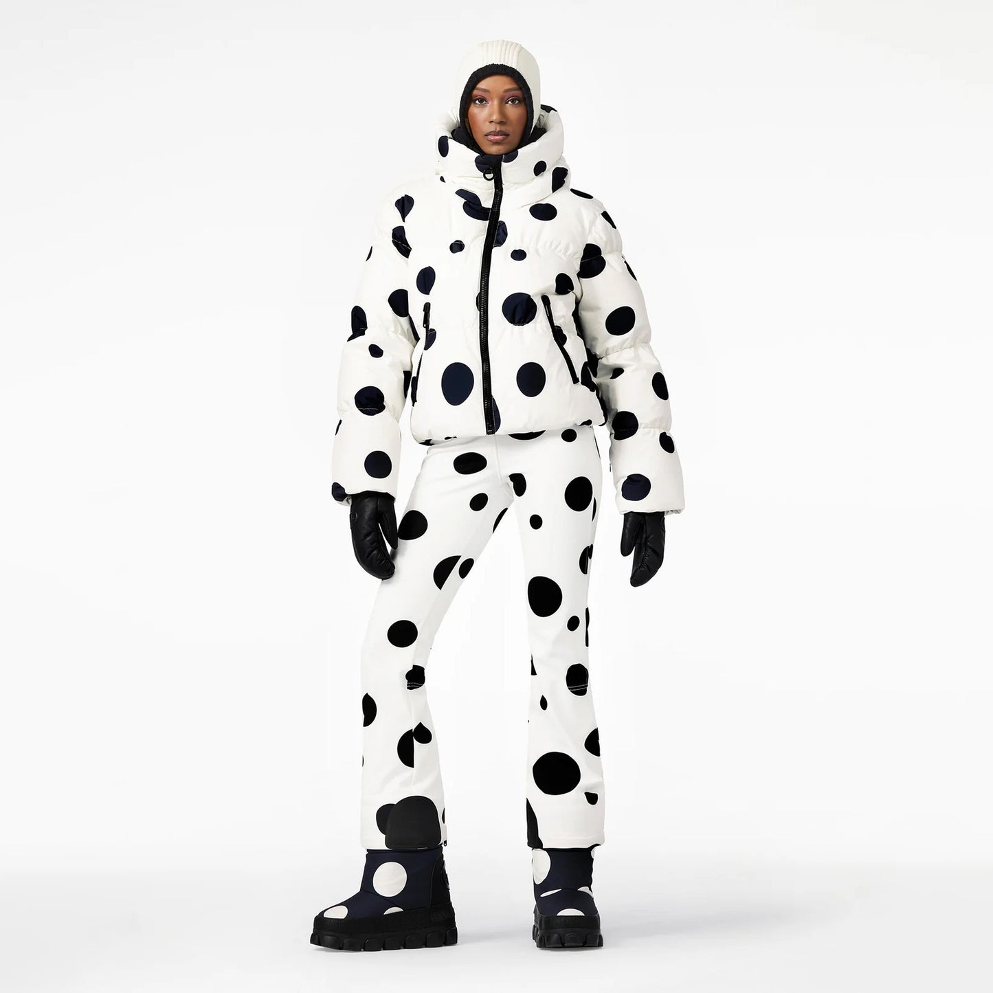 A person in the Goldbergh Grand Ski Jacket, Dot Cream, paired with matching ski pants, beanie, gloves, and waterproof boots stands against a plain backdrop.