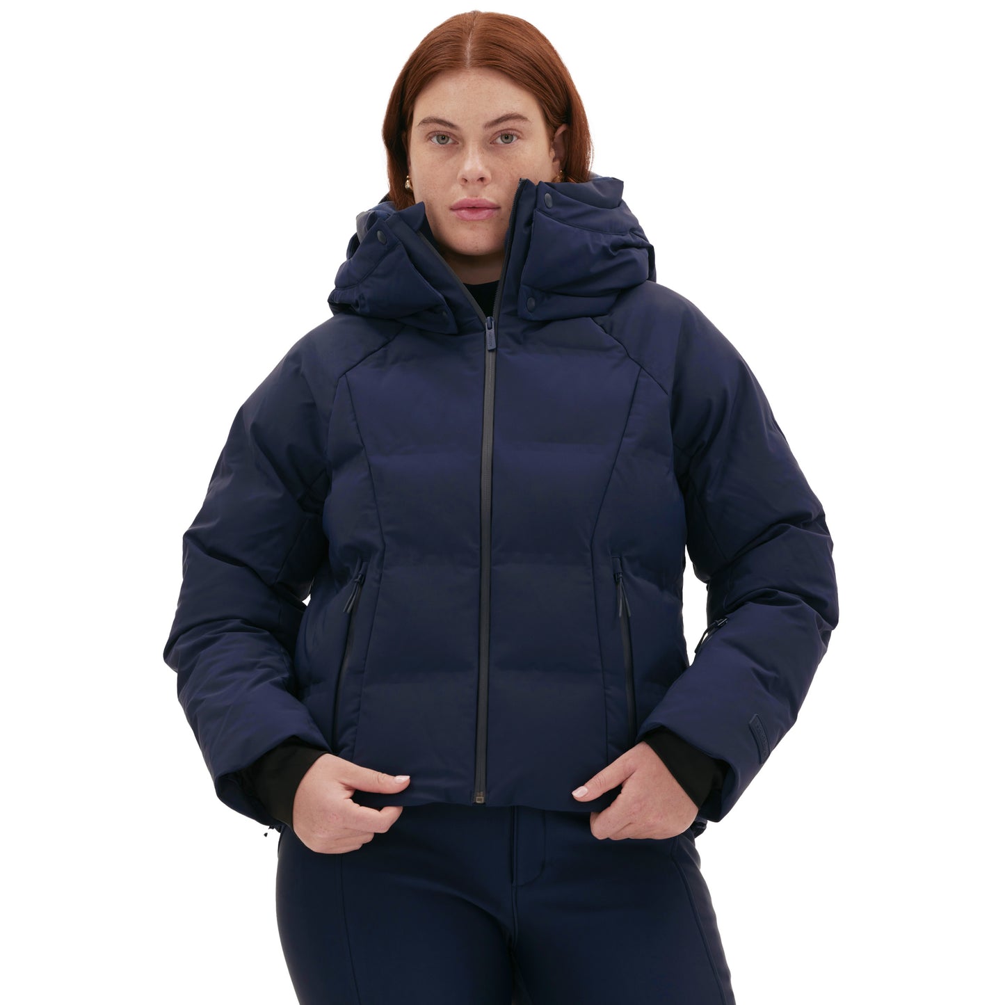 A person wearing Halfdays' Georgie Puffer Jacket in navy, featuring a hood, stands against a white background, ready for mountain performance on the slopes.