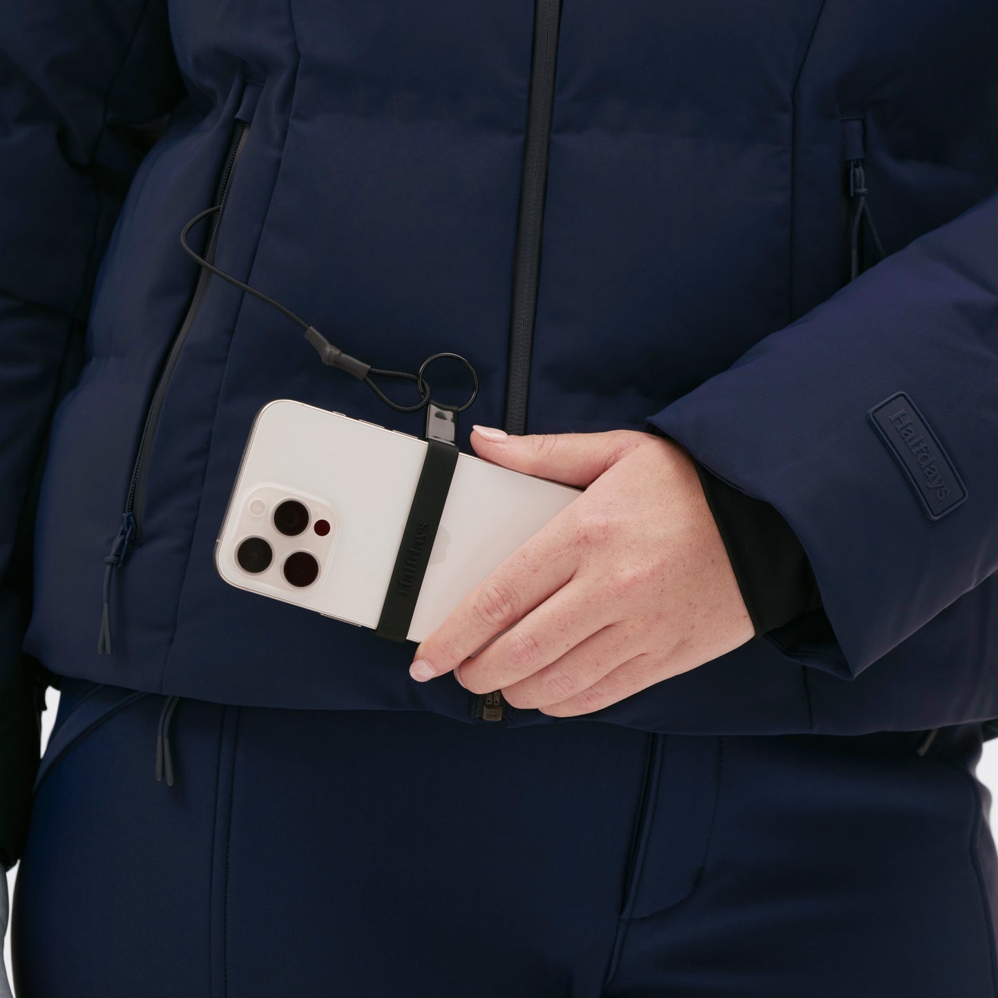 A person in a Georgie Puffer Jacket by Halfdays is holding a smartphone with a strap, ready for the slopes.