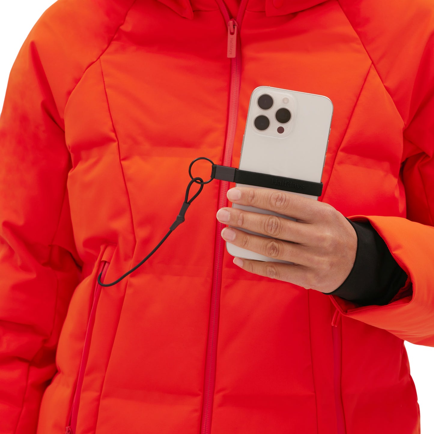 Wearing a Georgie Puffer Jacket by Halfdays, someone holds a smartphone securely with a strap attached to their hand, poised for the slopes.