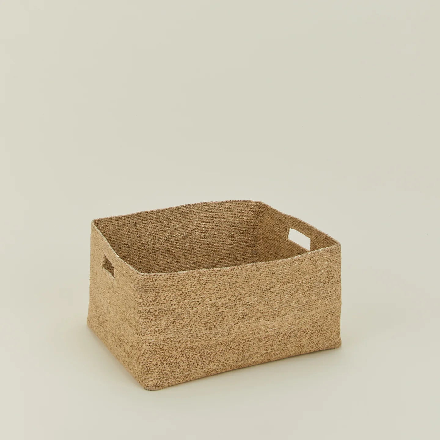 The Essential Low Basket by Hawkins New York is handwoven from seagrass, features two side handles, and is ideal for storing blankets or reducing clutter on any plain light background.