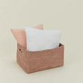 The Essential Low Basket from Hawkins New York, handwoven from seagrass, holds a white and light pink pillow—ideal for storing blankets or reducing clutter—set against a plain beige backdrop.