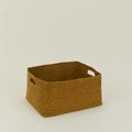 The Essential Low Basket by Hawkins New York is a rectangular handwoven seagrass basket with side handles, ideal for storing blankets and reducing clutter, shown on a plain light-colored surface.