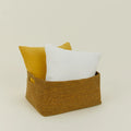 The Essential Low Basket by Hawkins New York, a rectangular handwoven seagrass piece, holds one white and one yellow pillow against a plain light background—ideal for minimizing clutter.