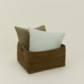 The Essential Low Basket by Hawkins New York holds a light grey pillow and a darker grey pillow, ideal for minimizing clutter, all set against a plain light background.