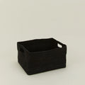 The Essential Low Basket by Hawkins New York is a handwoven black rectangular seagrass basket with side handles, ideal for storing blankets and reducing clutter, shown on a plain light-colored surface.