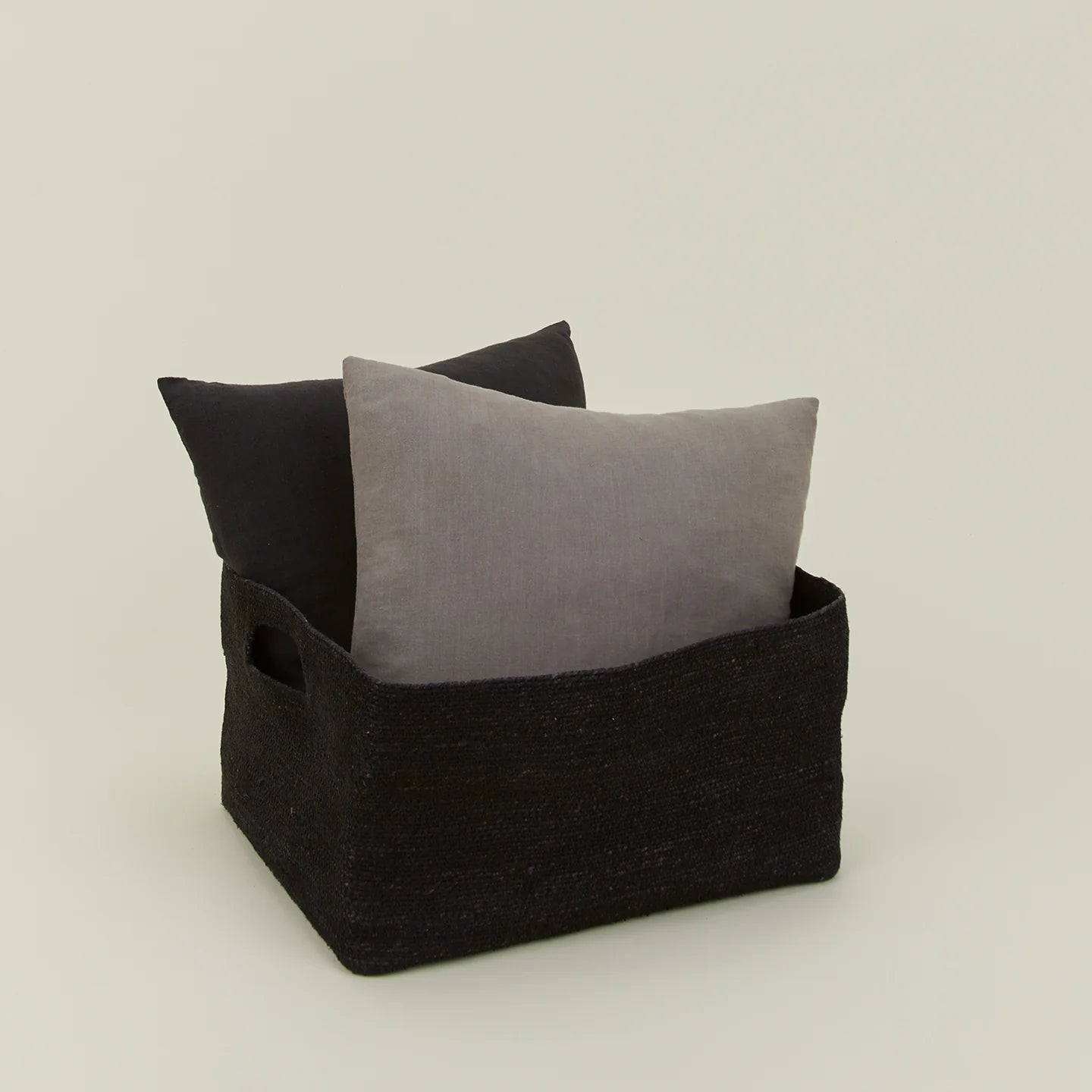 The Essential Low Basket by Hawkins New York holds two square pillows (dark and light gray) against a plain background—ideal for minimizing clutter or storing blankets stylishly.