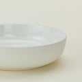 The Essential Low Bowl (Set of 4) by Hawkins New York is shown against a light beige background. Made from stoneware, these plain white bowls are dishwasher and microwave safe—ideal for everyday use.