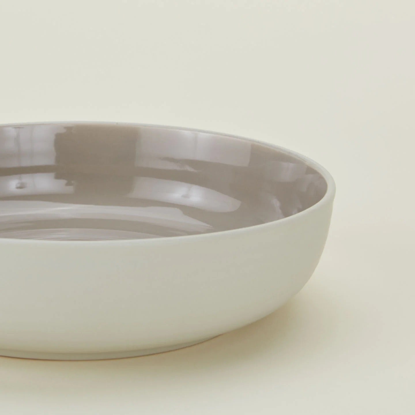 The Essential Low Bowl (Set of 4) by Hawkins New York features a round stoneware design with a glossy light gray interior and matte white exterior. Microwave and dishwasher safe, these bowls offer everyday convenience against any setting.