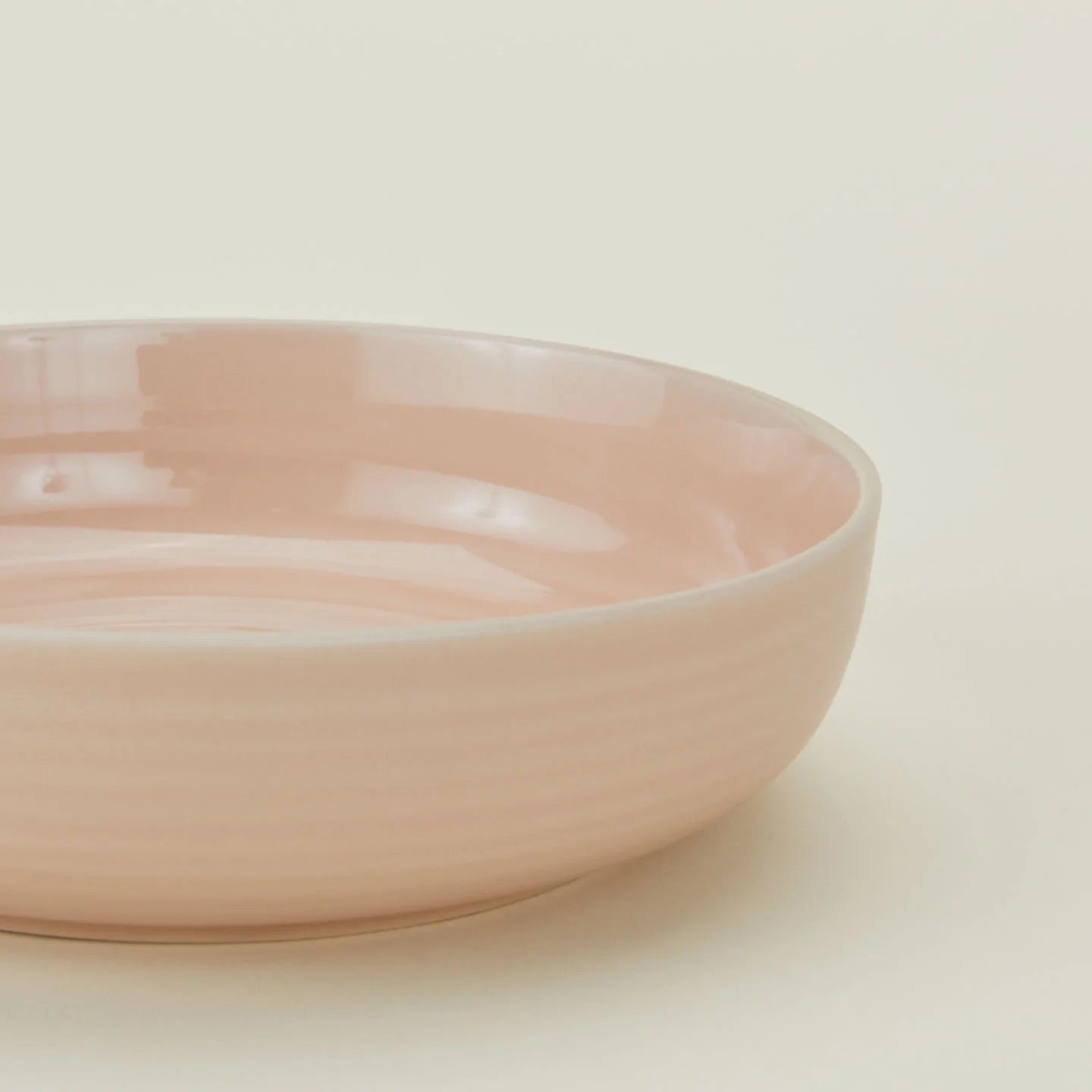 The Essential Low Bowl (Set of 4) by Hawkins New York features shallow, round, light pink stoneware bowls, microwave safe for convenience and perfect for elevating any table setting. Shown here on a plain off-white surface from a side angle.
