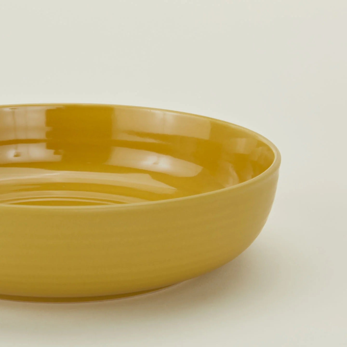 The Hawkins New York Essential Low Bowl (Set of 4) features round, shallow, mustard-yellow stoneware bowls, shown partially visible against a plain light background.