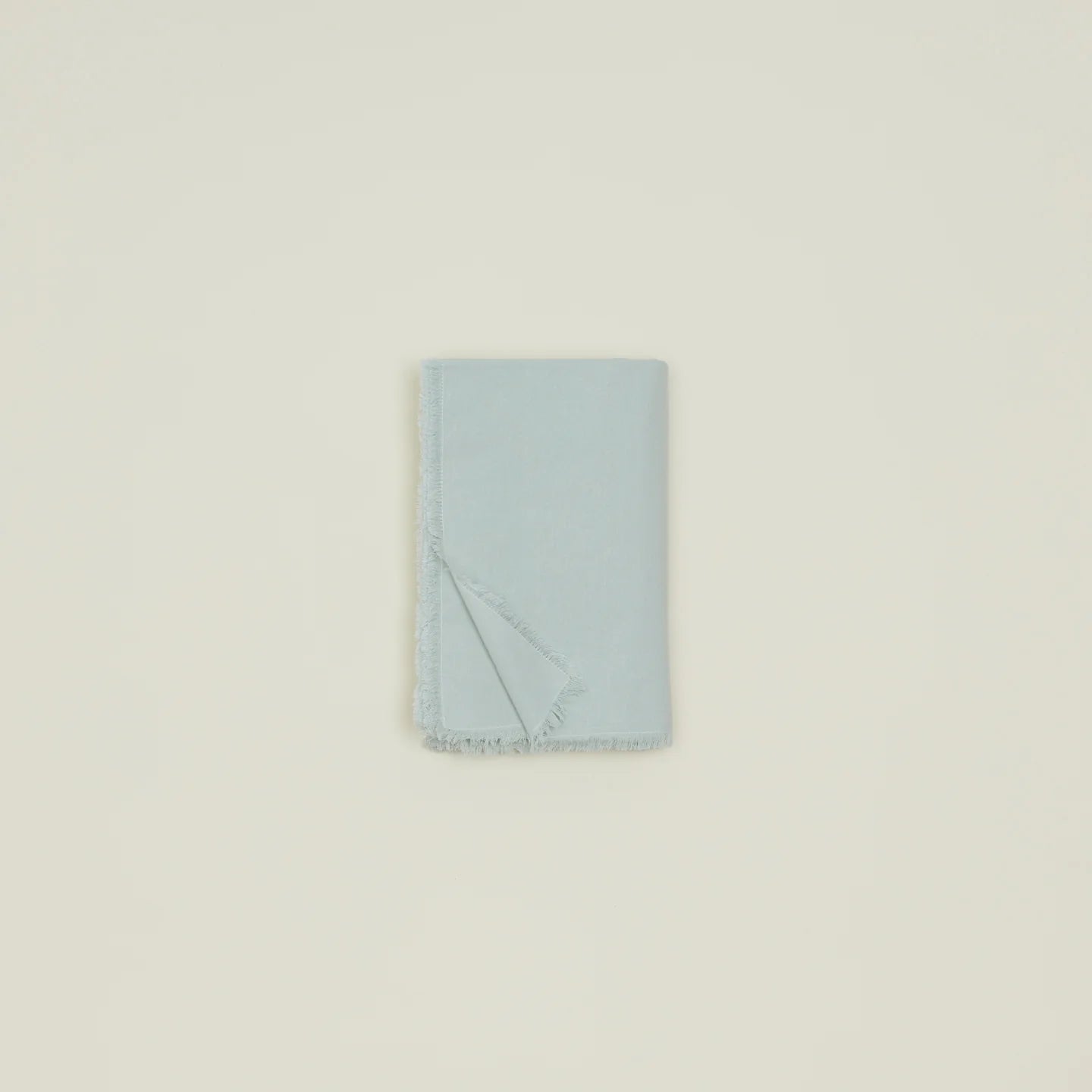 The Hawkins Essential Table Cloth Sky by Hawkins New York is neatly folded, featuring a soft fringed edge, and displayed on a plain off-white background.