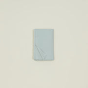 The Hawkins Essential Table Cloth Sky by Hawkins New York is neatly folded, featuring a soft fringed edge, and displayed on a plain off-white background.