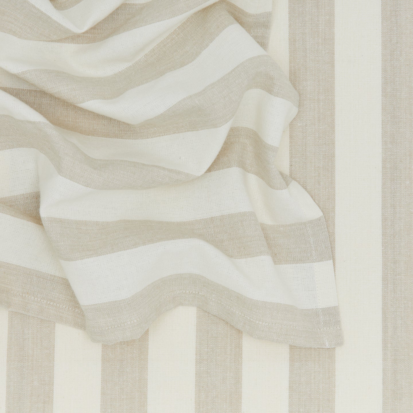 These beige and white striped placemats from Hawkins New York's Essential Collection feature partially draped folds, perfect for embodying an easy living vibe.